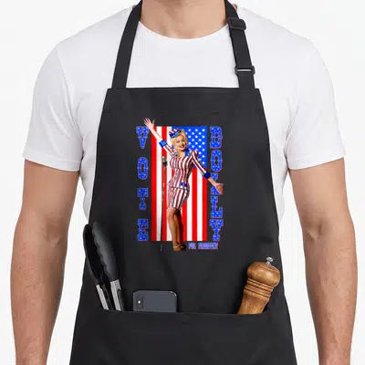 President dolly parton apron - Woman in patriotic suit with VOTE DOTLY FOR PRESIDENT text and USA flag background — shown on a black cotton canvas apron against a white background