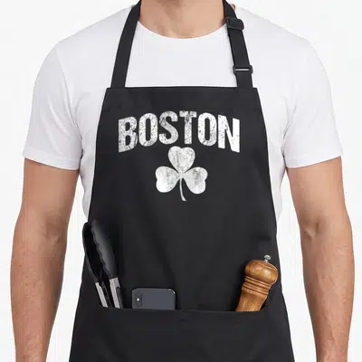 Distressed st patrick day aprons - Arched white BOSTON text above a distressed shamrock on dark canvas — shown on a black cotton canvas apron against a white background