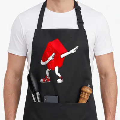 Dabbing master block & apron - Red toy brick character with white limbs and red shoes dabbing in cartoon style — shown on a black cotton canvas apron against a white background
