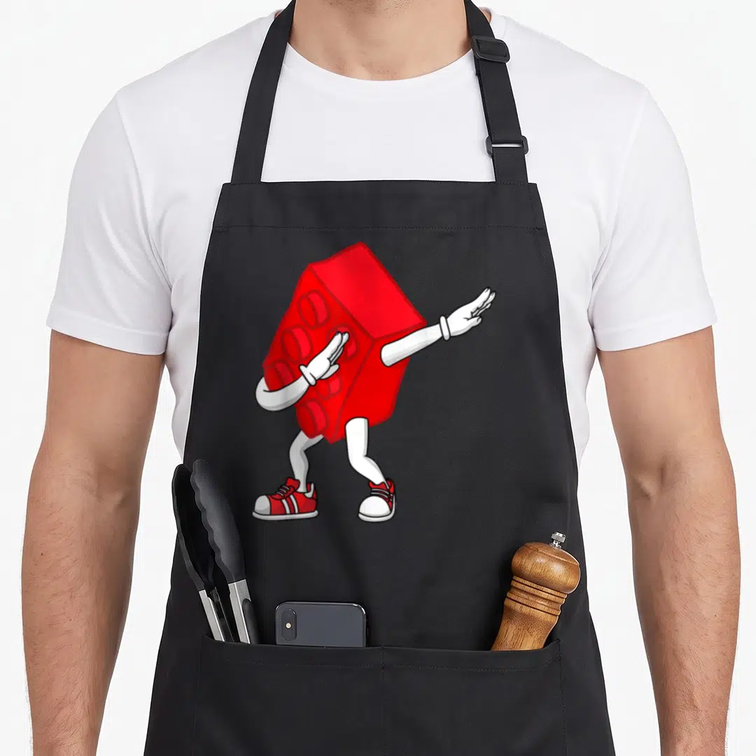 Dabbing master block & apron - Red toy brick character with white limbs and red shoes dabbing in cartoon style — shown on a black cotton canvas apron against a white background