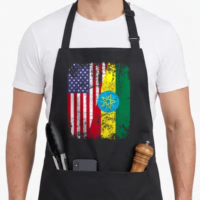Ethiopian american flag apron - Two flags merged side-by-side with distressed weathered texture in red white blue green — shown on a black cotton canvas apron against a white background