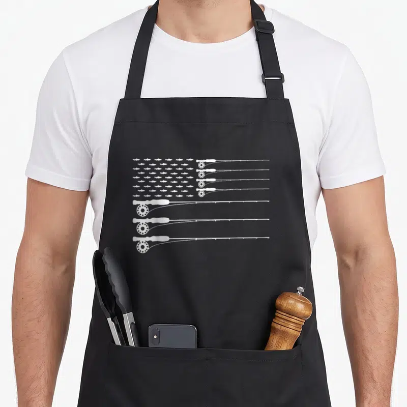 Trout american flag apron - White fishing rods and fish silhouettes arranged in a US flag shape — shown on a black cotton canvas apron against a white background