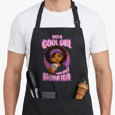 Kawaii boba anime apron - Cartoon girl with afro hair holding boba tea cup under pink and purple text — shown on a black cotton canvas apron against a white background