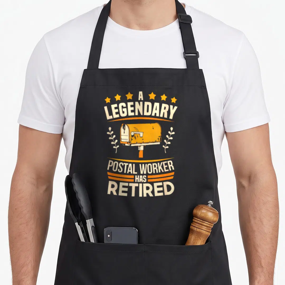 Retiree postal aprons - Orange mailbox with stars and leaves surrounding text A LEGENDARY POSTAL WORKER HAS RETIRED — shown on a black cotton canvas apron against a white background