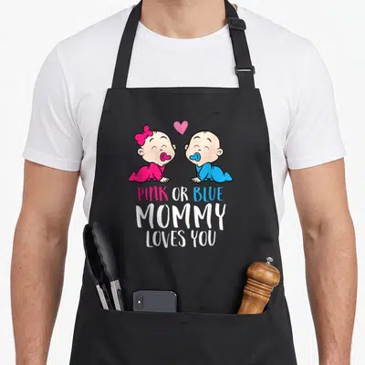 Pregnancy apron or apron - Two cartoon babies in pink and blue facing each other with heart and stacked text PINK — shown on a black cotton canvas apron against a white background