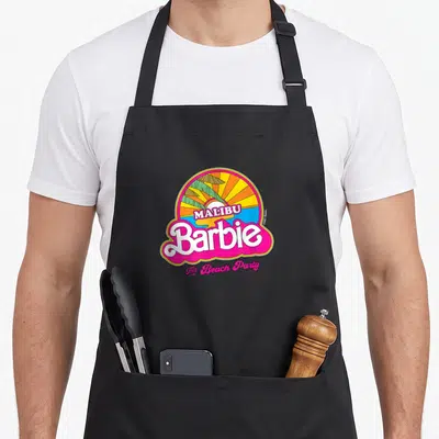 Malibu barbiecore apron - Retro sun graphic with palm trees and pink bubble text reading Malibu Barbie The Beach Party — shown on a black cotton canvas apron against a white background