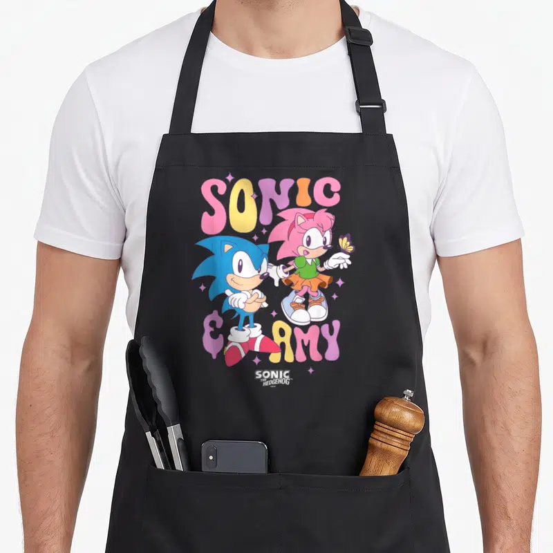 Amy hedgehog mom apron - Sonic and Amy cartoon with pink blue yellow purple text and butterfly — shown on a black cotton canvas apron against a white background