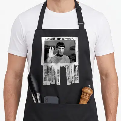 Original logic apron - Spock portrait with LOGIC OF SPOCK text and torn quote strips in black and white — shown on a black cotton canvas apron against a white background
