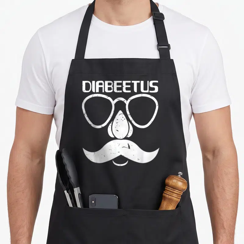 Diabete beard apron - White distressed DIABEETUS text above glasses nose and mustache forming face — shown on a black cotton canvas apron against a white background