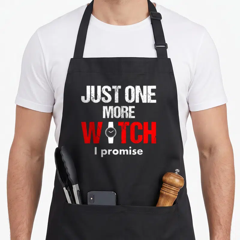 Collector watching funny apron - Distressed text JUST ONE MORE WATCH I promise with white watch icon replacing A in red — shown on a black cotton canvas apron against a white background