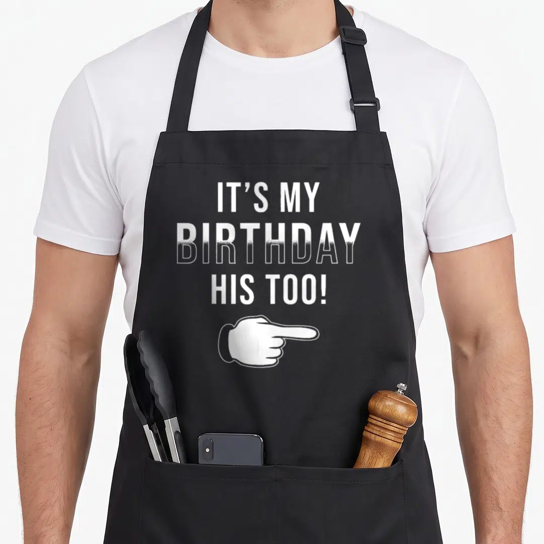 Twin his birthday apron - White stacked text It's My Birthday His Too! with pointing hand on black bib — shown on a black cotton canvas apron against a white background