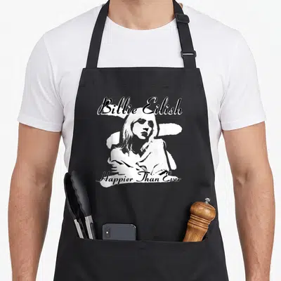 Eilish black apron - Distressed black and white portrait of a woman with Billie Eilish and Happier Than Ever text — shown on a black cotton canvas apron against a white background