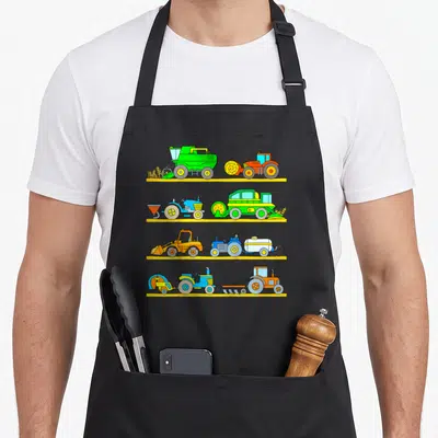 Combine vehicle apron - Eight cartoon farm vehicles on four yellow shelves in green orange blue and yellow — shown on a black cotton canvas apron against a white background
