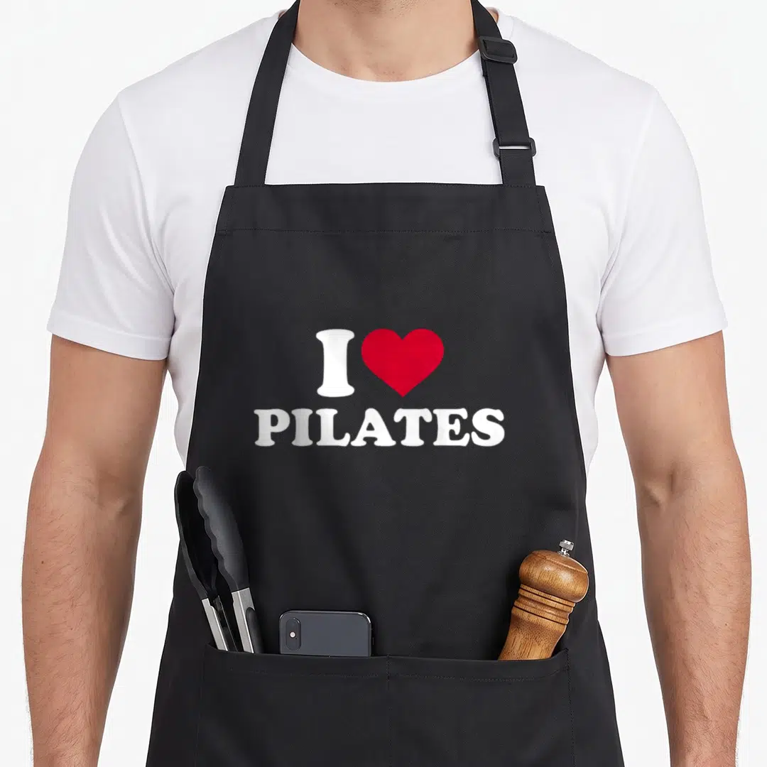 Cool pilates apron - White letter I, red heart, and white Pilates text stacked vertically — shown on a black cotton canvas apron against a white background