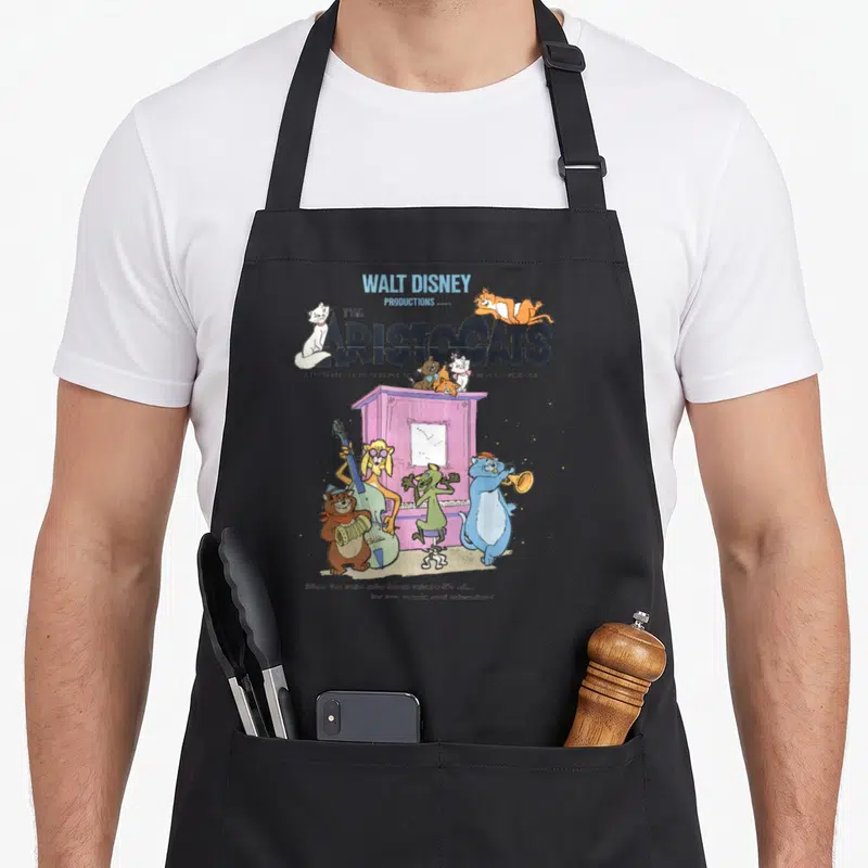 Aristocat piano apron - Vintage Aristocats title with cats playing instruments around a purple piano — shown on a black cotton canvas apron against a white background