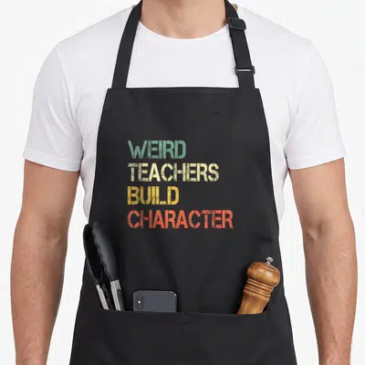 Weird classroom aprons - Stacked distressed text reading WEIRD TEACHERS BUILD CHARACTER in teal beige yellow and orange — shown on a black cotton canvas apron against a white background