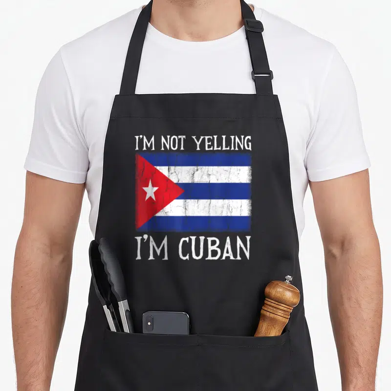 Yelling cuban apron - Distressed Cuba flag with white text reading I'm not yelling I'm Cuban centered on black fabric — shown on a black cotton canvas apron against a white background