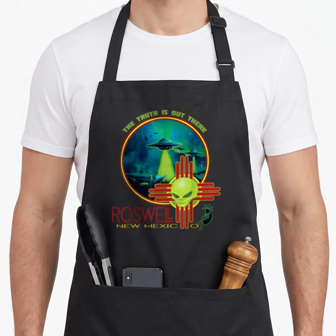 Roswell mexico apron - Alien head over red Zia symbol with UFOs and The Truth Is Out There text — shown on a black cotton canvas apron against a white background