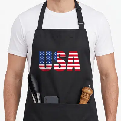 Funny usa flag apron - USA text filled with red white and blue flag pattern — shown on a black cotton canvas apron against a white background
