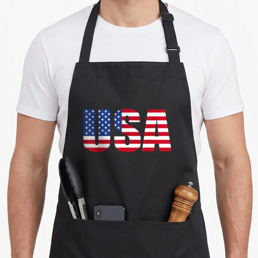 Funny usa flag apron - USA text filled with red white and blue flag pattern — shown on a black cotton canvas apron against a white background
