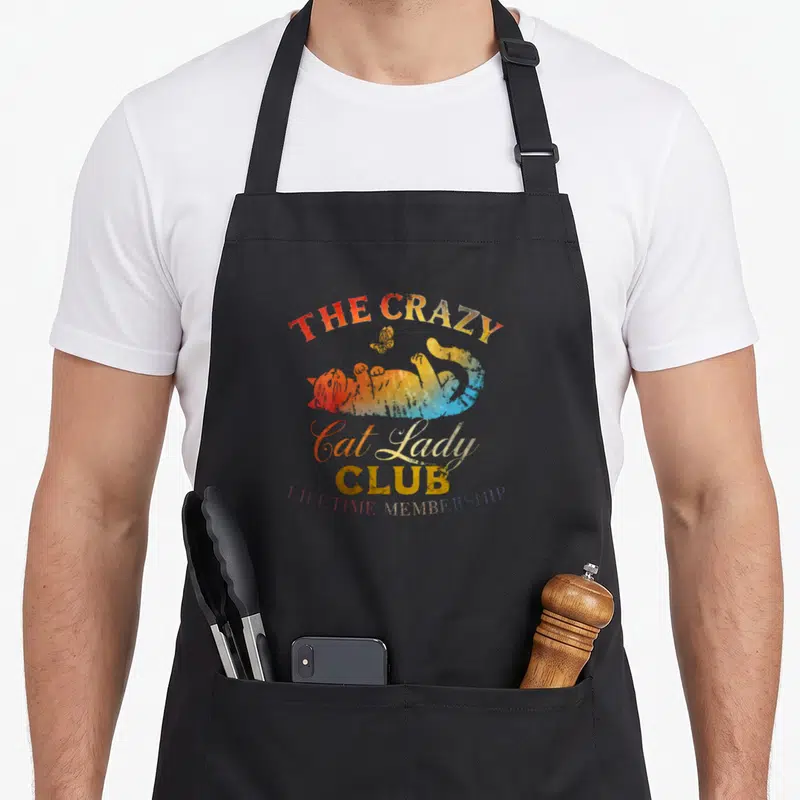 Lifetime crazy cat lady apron - Rainbow watercolor cat lying down with THE CRAZY Cat Lady CLUB Lifetime Membership text — shown on a black cotton canvas apron against a white background