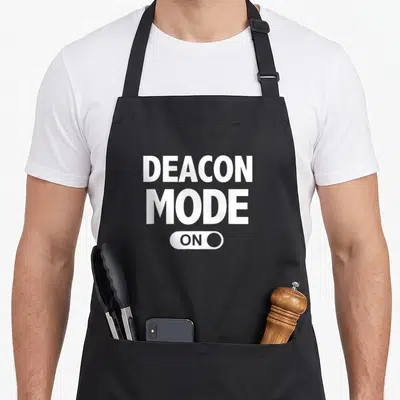 Deacon christian apron - White DEACON MODE ON text with toggle switch graphic on grey background — shown on a black cotton canvas apron against a white background