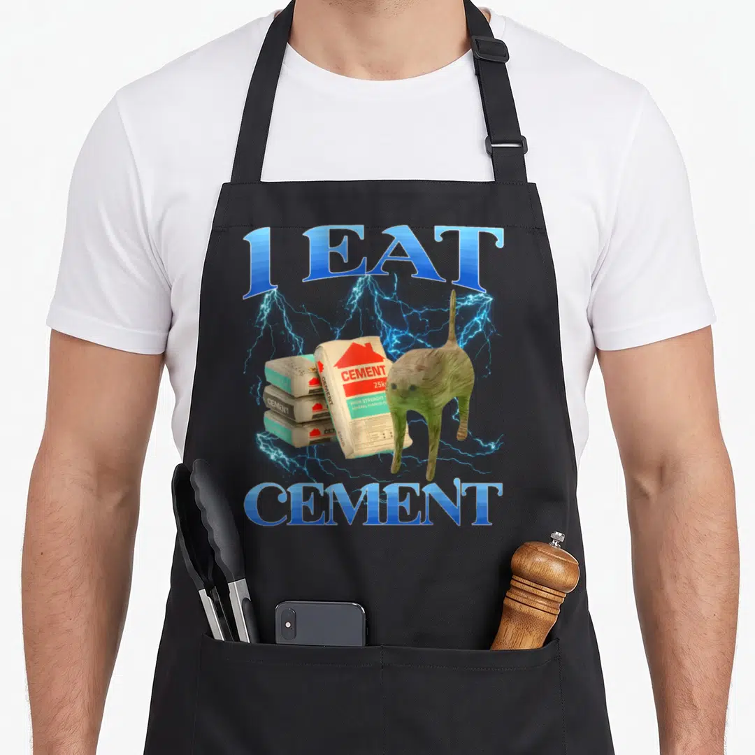 Eat cat apron - I EAT CEMENT text with tan cat, three cement bags, blue lightning, grey clouds — shown on a black cotton canvas apron against a white background