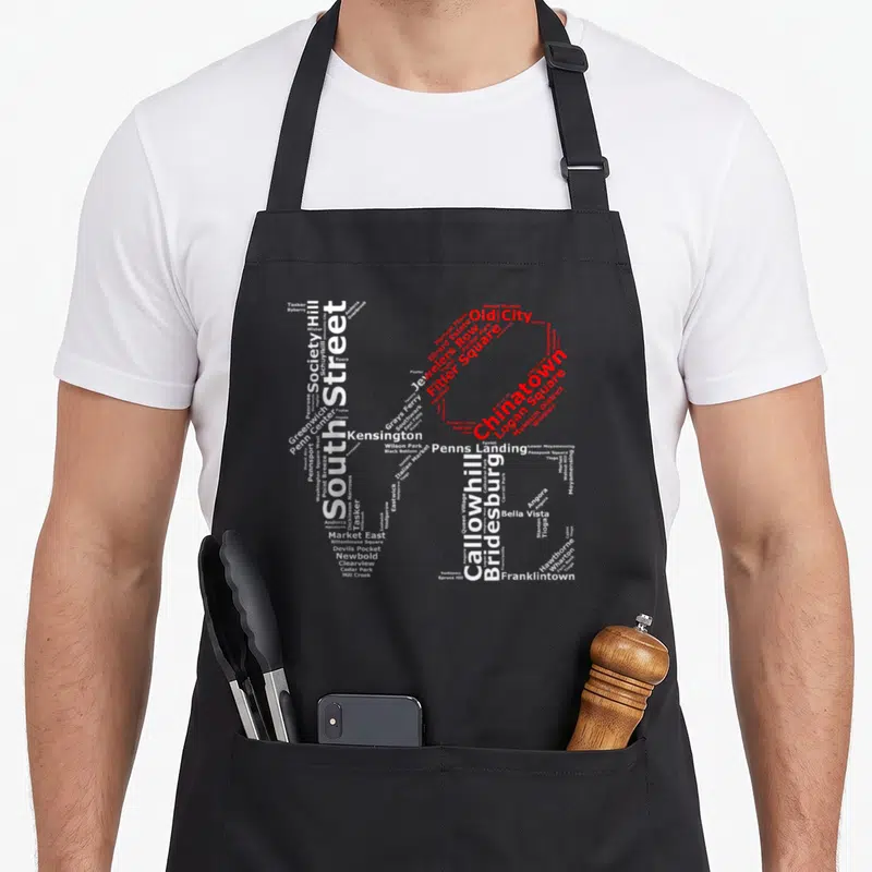 Park phillies apron - PH monogram formed by neighborhood names like Chinatown and South Street in white and red — shown on a black cotton canvas apron against a white background