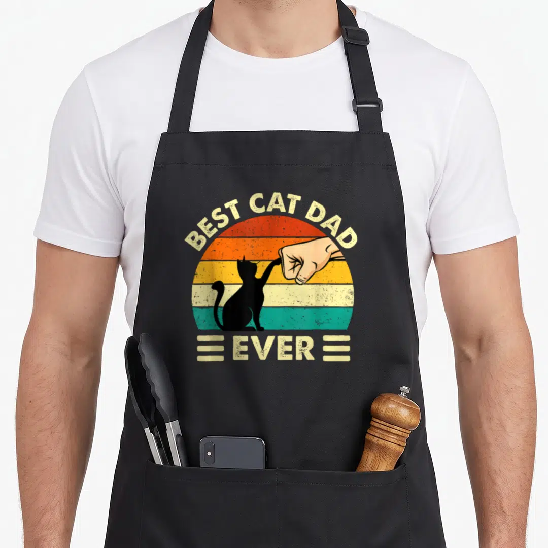 Owner kitty cat apron - Retro sun graphic with black cat fist bumping human hand and text BEST CAT DAD EVER — shown on a black cotton canvas apron against a white background