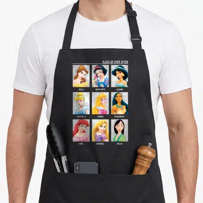 Class princess apron - Nine princess portraits in a grid with names Belle Snow White Jasmine Cinderella Aurora — shown on a black cotton canvas apron against a white background