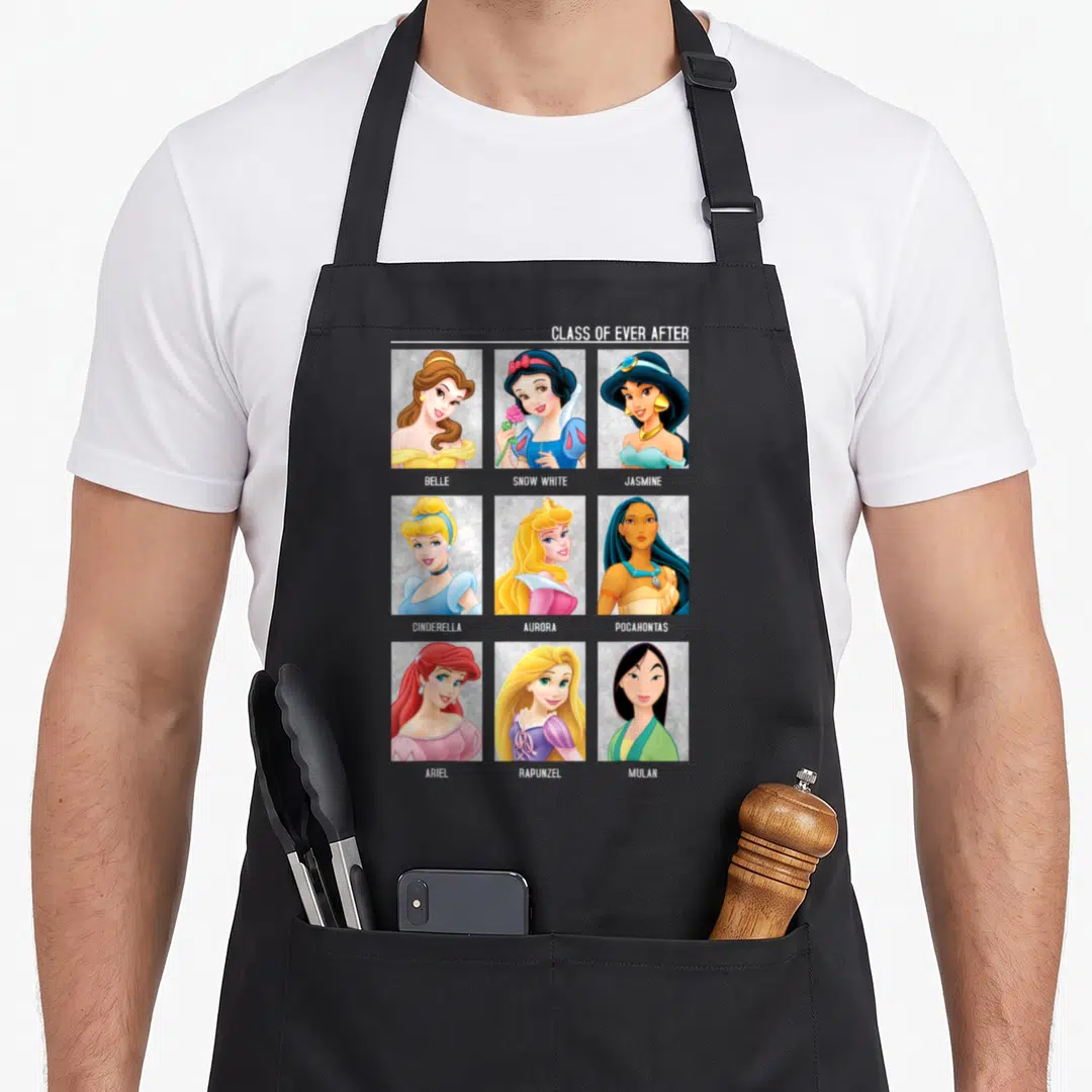 Class princess apron - Nine princess portraits in a grid with names Belle Snow White Jasmine Cinderella Aurora — shown on a black cotton canvas apron against a white background