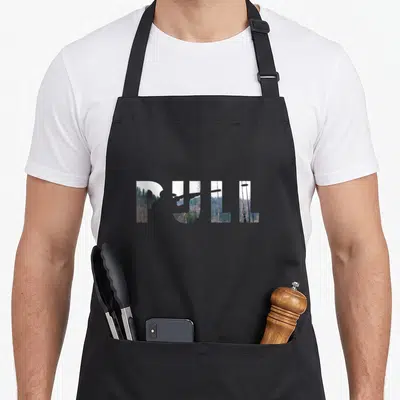Pull trap shooting apron - PULL text filled with green and brown forest photography image — shown on a black cotton canvas apron against a white background