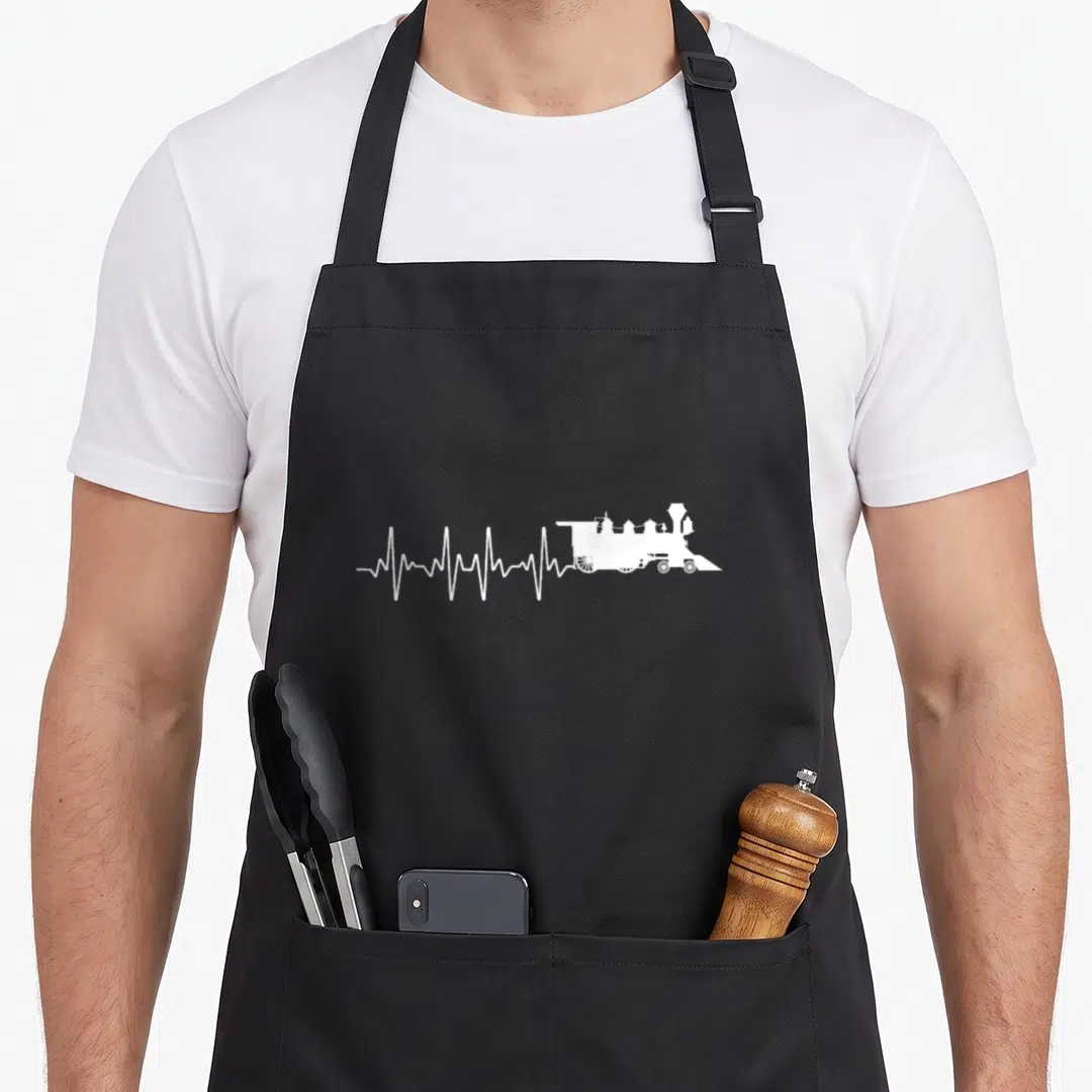 Train model apron - White steam locomotive facing right connected to a white heartbeat line on grey background — shown on a black cotton canvas apron against a white background