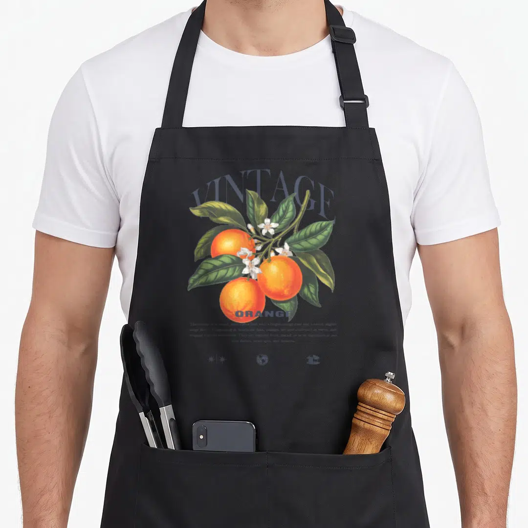 Food fun apron - VINTAGE ORANGE botanical print with three citrus fruits, green leaves, white flowers and descriptive — shown on a black cotton canvas apron against a white background