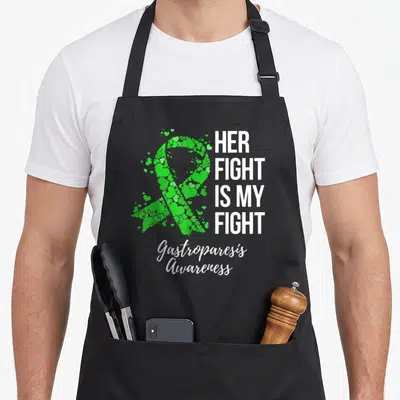 Funny fight gastroparesis awareness apron - Green ribbon made of hearts next to white text HER FIGHT IS MY FIGHT — shown on a black cotton canvas apron against a white background