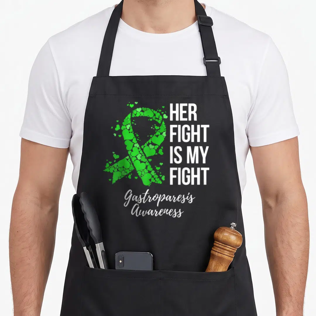 Funny fight gastroparesis awareness apron - Green ribbon made of hearts next to white text HER FIGHT IS MY FIGHT — shown on a black cotton canvas apron against a white background