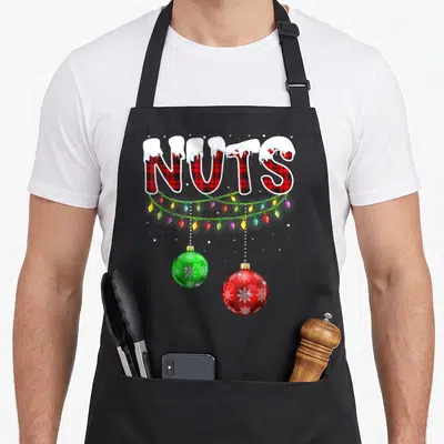 Cute nut couples christmas aprons - NUTS text in red plaid with snow, multicolored lights, and two hanging baubles — shown on a black cotton canvas apron against a white background