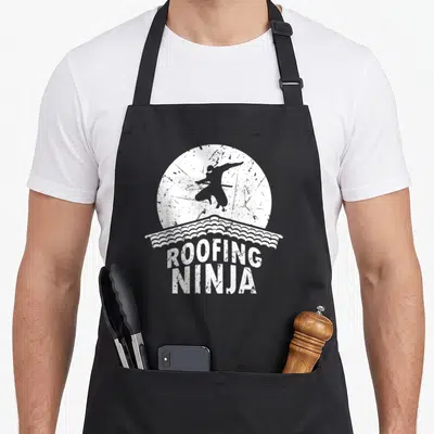 Slating roofing apron - Ninja silhouette in white circle above roof tiles with distressed ROOFING NINJA text — shown on a black cotton canvas apron against a white background