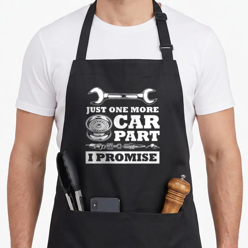 Owner car apron - White wrench and wheel rim with stacked text JUST ONE MORE CAR PART I PROMISE — shown on a black cotton canvas apron against a white background