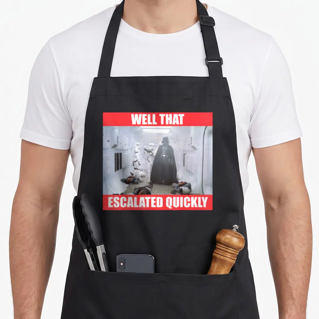 Well general apron - Darth Vader in white corridor with red banners reading Well That Escalated Quickly — shown on a black cotton canvas apron against a white background