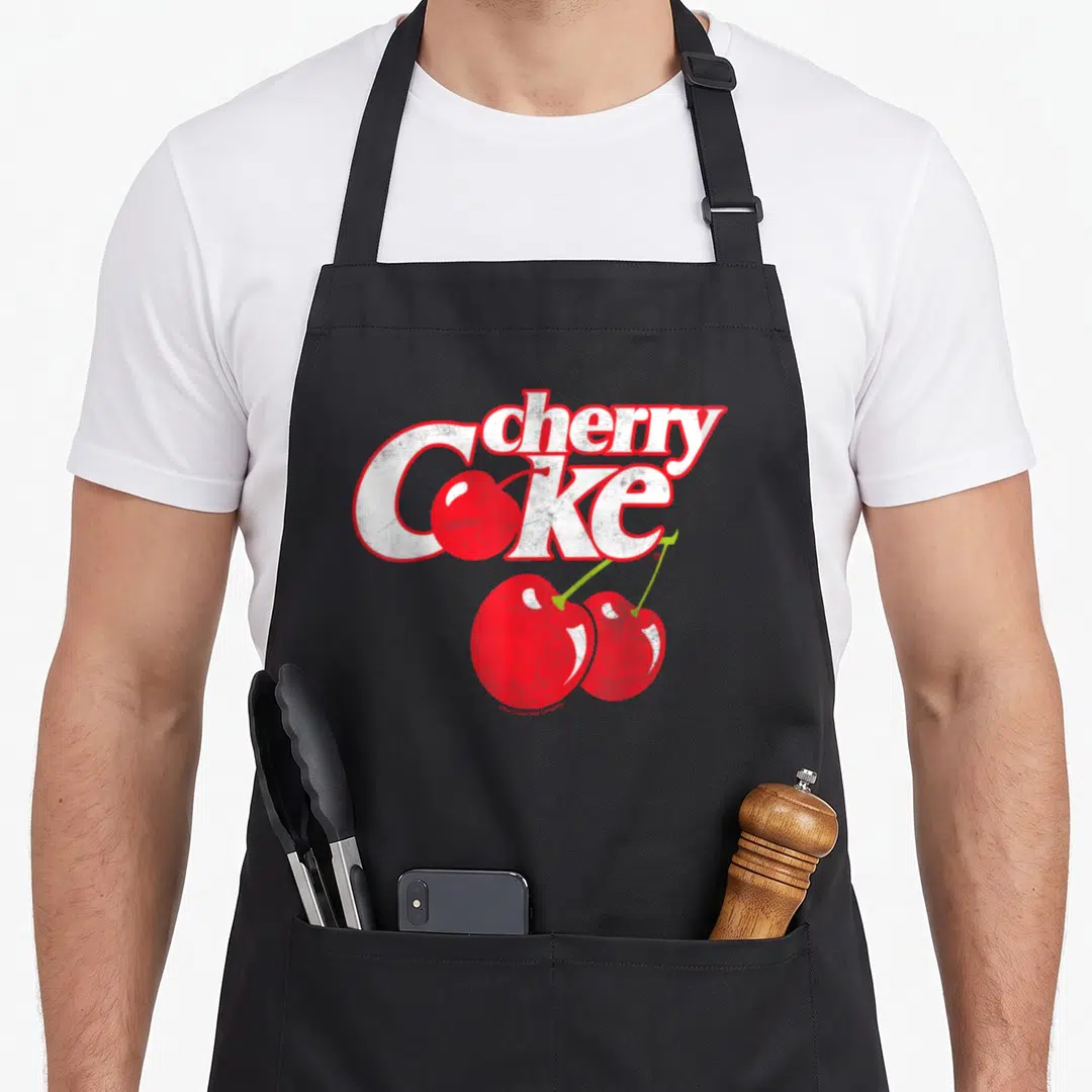 Coca cherry apron - Distressed cherry Coke text with red cherries and green stems — shown on a black cotton canvas apron against a white background