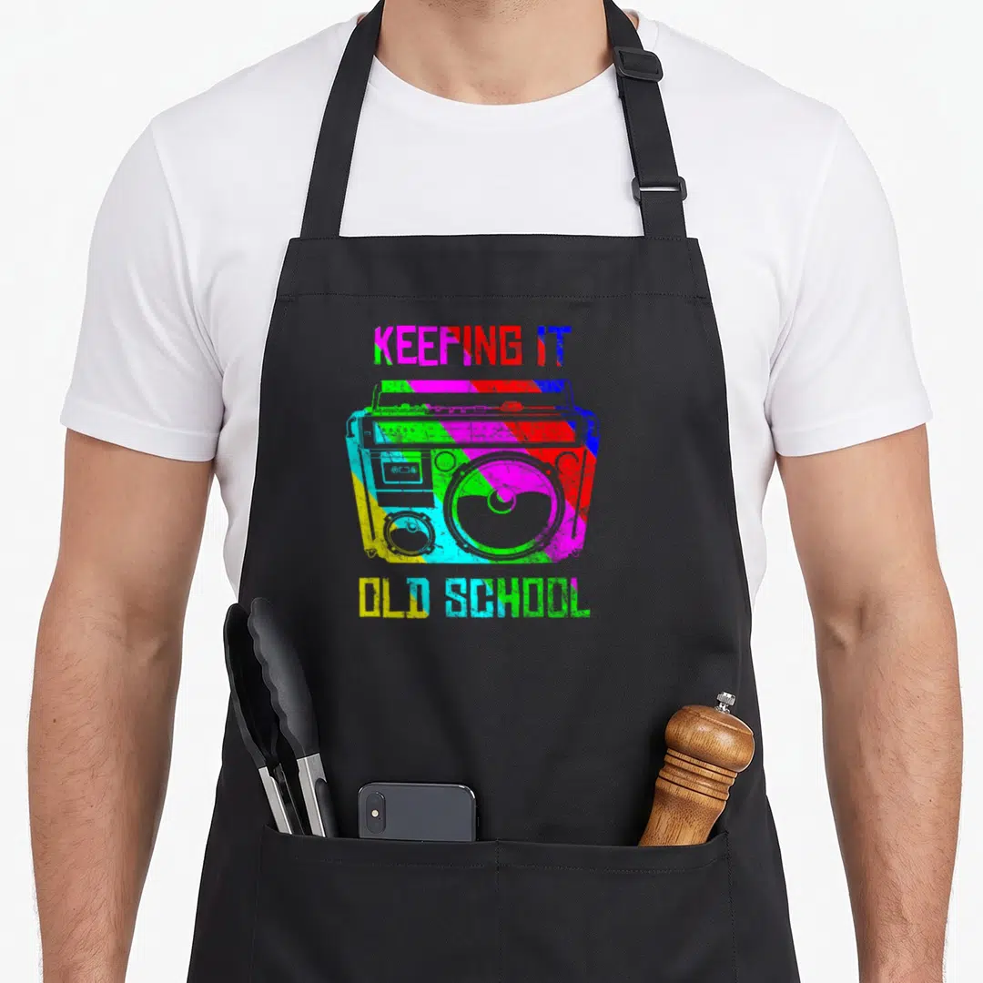 Keeping school 80s apron - Colorful striped boombox with KEEPING IT OLD SCHOOL text in retro font — shown on a black cotton canvas apron against a white background