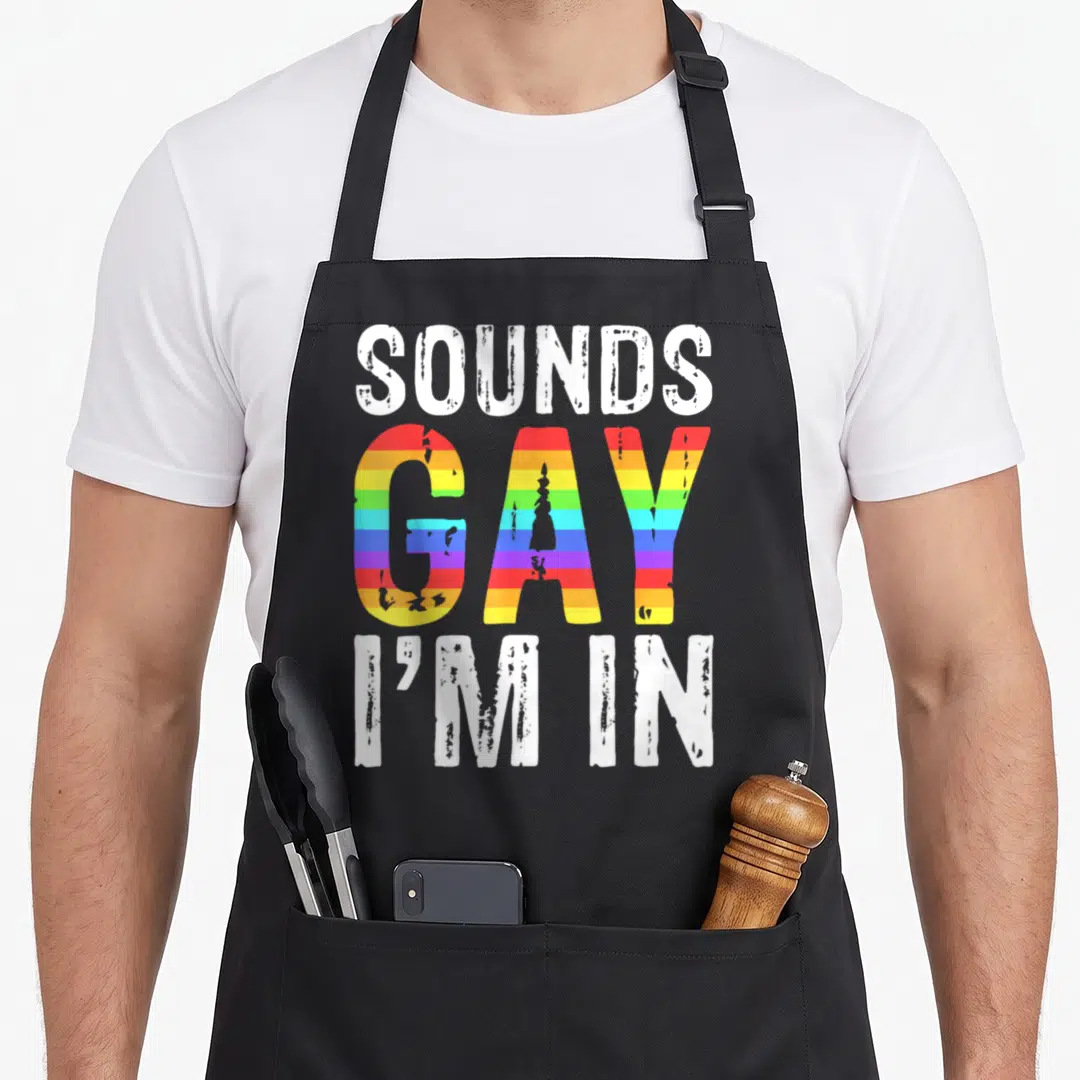 Sound lgbt gay pride apron - SOUNDS GAY I'M IN text with rainbow striped GAY lettering on white background — shown on a black cotton canvas apron against a white background