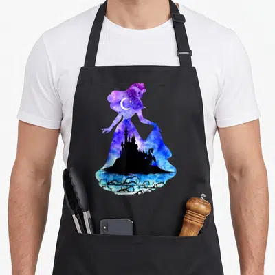 Castle beauty apron - Galaxy woman silhouette with black castle, dragon, moon, and thorns in purple and blue watercolor — shown on a black cotton canvas apron against a white background
