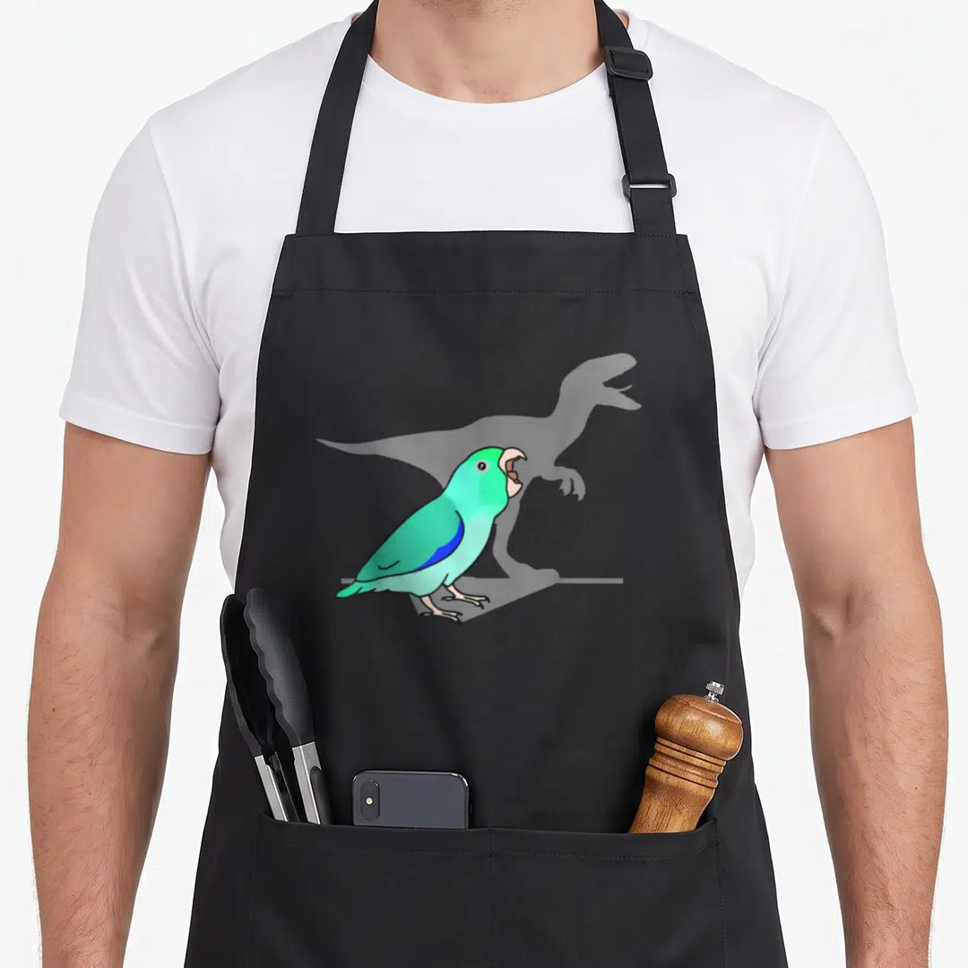 Velociraptor meme apron - Teal cartoon parrot standing before a grey dinosaur silhouette in profile view — shown on a black cotton canvas apron against a white background