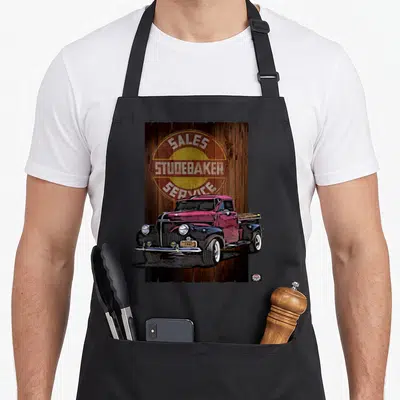 Pickup studebaker by rm auto art apron - Maroon 1947 truck in front of Sales Studebaker Service circular sign on wood — shown on a black cotton canvas apron against a white background
