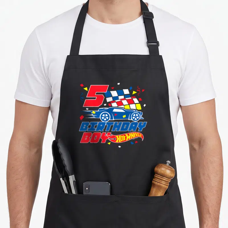 5th wheel apron - Red number 5, blue race car, checkered flag, and birthday boy text with confetti — shown on a black cotton canvas apron against a white background