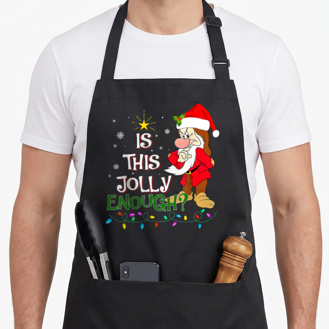 Jolly christmas lights apron - Grumpy Santa points next to Is This Jolly Enough text and string lights — shown on a black cotton canvas apron against a white background