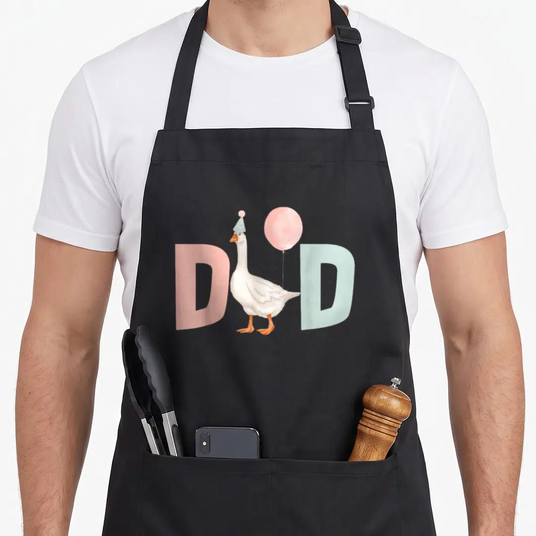 1st silly apron - White goose in party hat holding balloon between pink and blue D letters — shown on a black cotton canvas apron against a white background