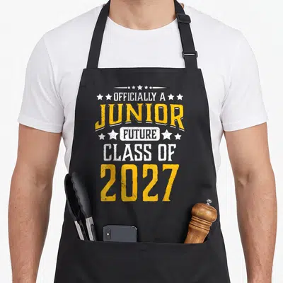 Officially junior apron - Distressed yellow and white text reading OFFICIALLY A JUNIOR FUTURE CLASS OF 2027 — shown on a black cotton canvas apron against a white background